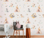 Cream kids wallpaper with deer, raccoons and teepees in nursery with grey chair and crib