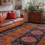 A vibrant Crimson Flora Hand Knotted Area Rug in a cozy living room setting. This vintage rug features intricate Persian designs with rich orange and navy hues. Perfect for large living rooms, the area rug complements the warm tones of a leather sofa and adds a touch of elegance to the space. Lush greenery and natural light enhance the inviting atmosphere.