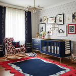 Nursery room with blue crib, colorful rug, and decorative wall art.
