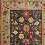 Elegant hand-knotted area rug featuring a vibrant floral pattern with rich, colorful blooms on a deep blue background, bordered by intricate floral designs in pastel hues.