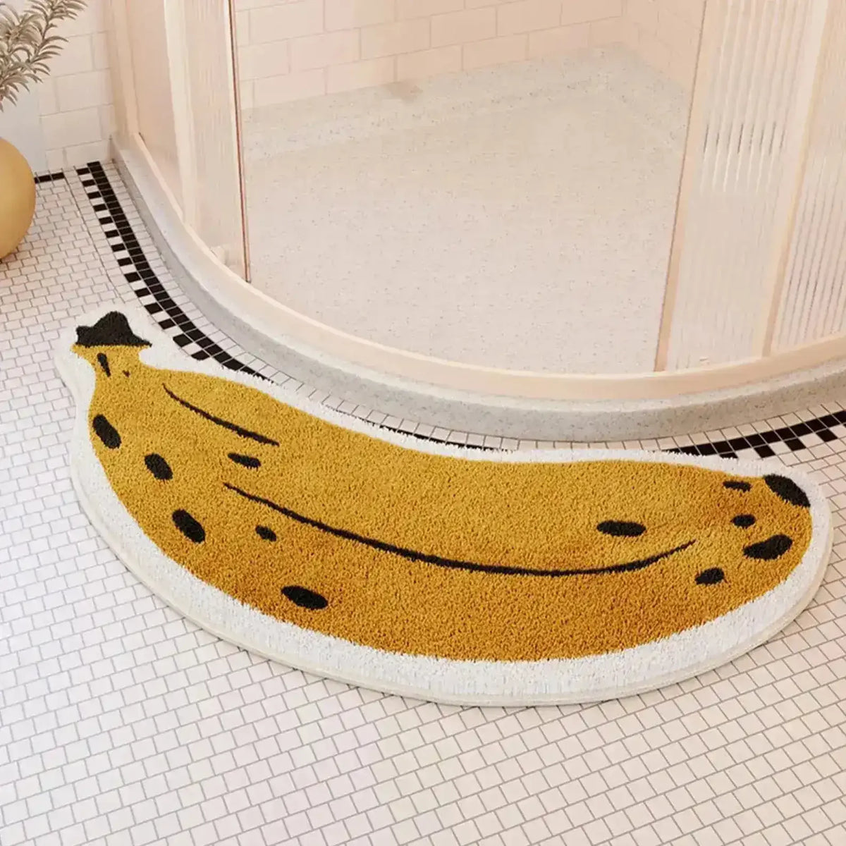 A charming banana-shaped area rug placed on a tiled bathroom floor, adding a playful touch to the decor. The rug features a vibrant yellow color with black detailing, enhancing the whimsical banana design.