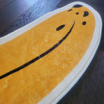 A charming area rug shaped like a banana, featuring a vibrant yellow hue and black detailing, placed on a dark wooden floor.