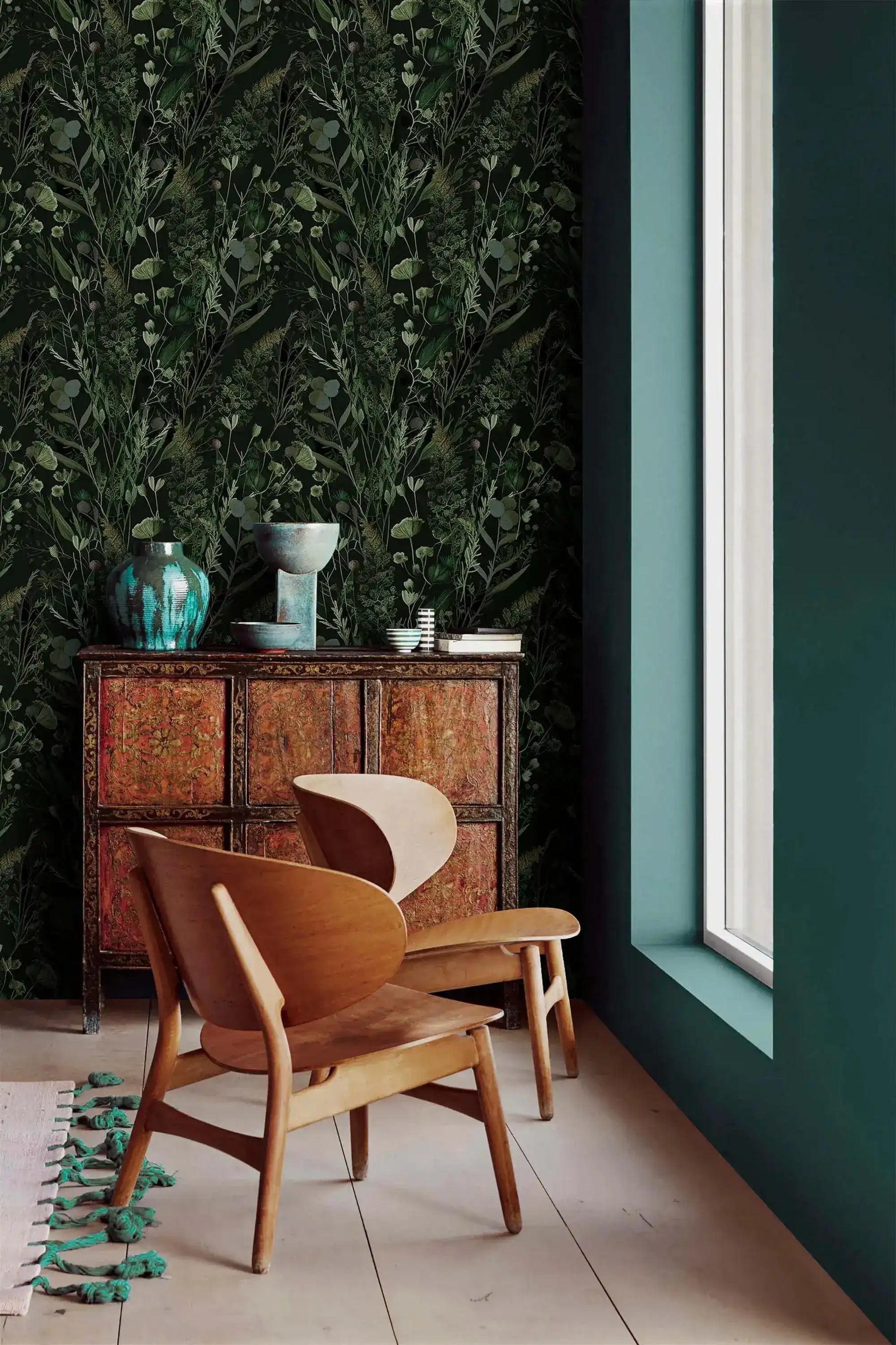 Dark fern wallpaper in corner with carved wood cabinet, teal vases and curved wooden lounge chair