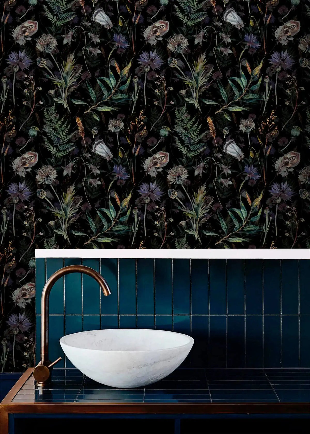 Dark floral fern wallpaper above blue tiled bathroom vanity with marble basin and brass tap