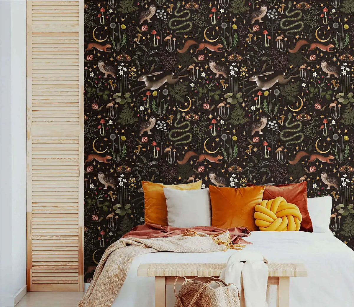 Enchanted Wilderness wallpaper as bedroom feature wall; amber and rust pillows on white bed, natural wood louvered door