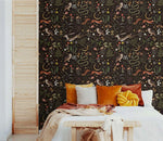 Enchanted Wilderness wallpaper as bedroom feature wall; amber and rust pillows on white bed, natural wood louvered door
