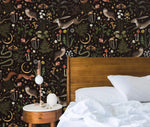 Enchanted Wilderness wallpaper in bedroom with walnut bed and white linens; hares, owls, snakes, moons on dark background