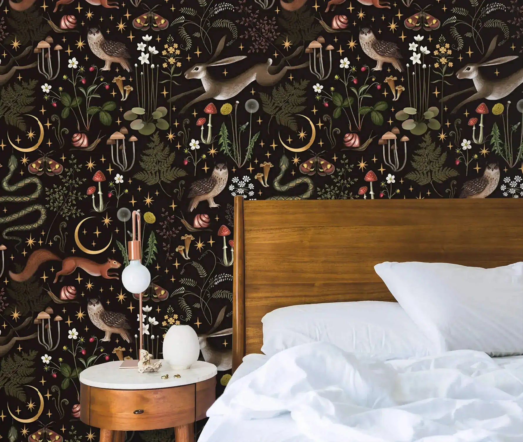 Enchanted Wilderness wallpaper in bedroom with walnut bed and white linens; hares, owls, snakes, moons on dark background