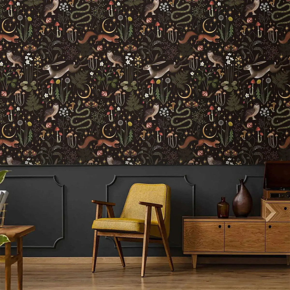 Enchanted Wilderness wallpaper above dark grey paneling; retro yellow armchair and oak sideboard in moody sitting room