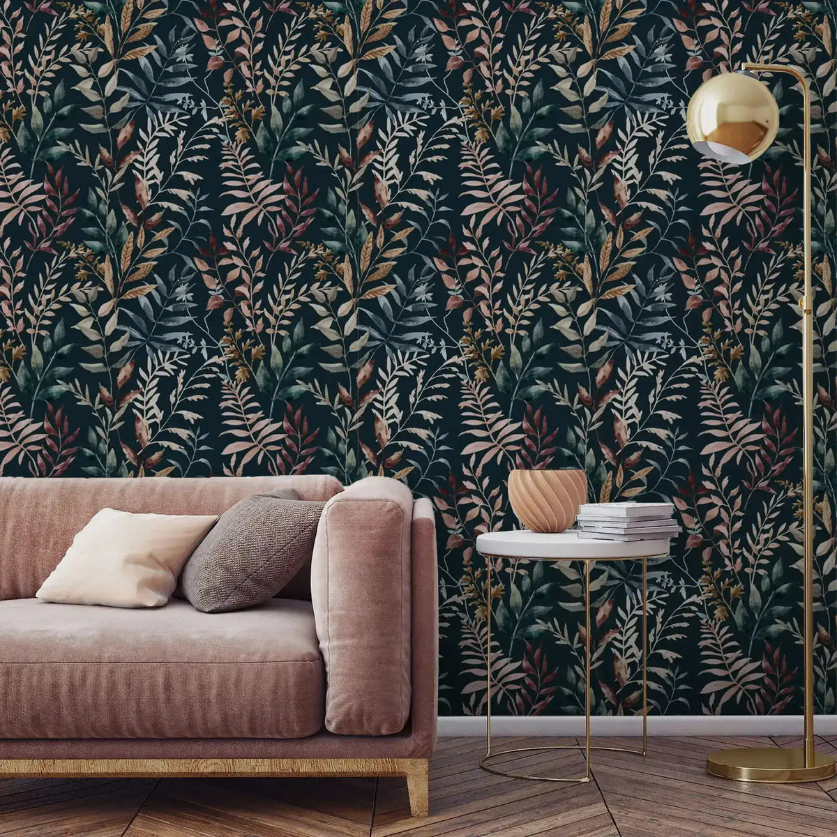 Dark navy botanical wallpaper with mixed-color leaves in living room setting with pink sofa and gold floor lamp.