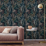 Dark navy botanical wallpaper with mixed-color leaves in living room setting with pink sofa and gold floor lamp.