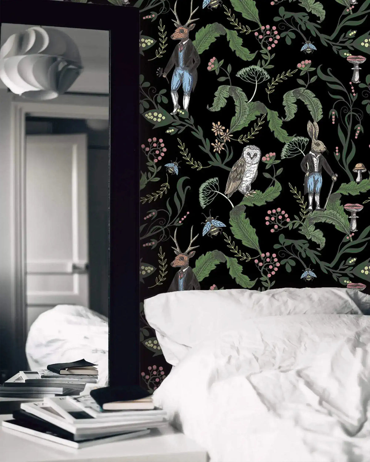 Dark woodland wallpaper with owls, a stag and hares on black in a moody bedroom with white linens