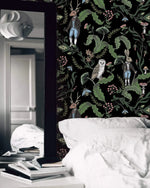 Dark woodland wallpaper with owls, a stag and hares on black in a moody bedroom with white linens