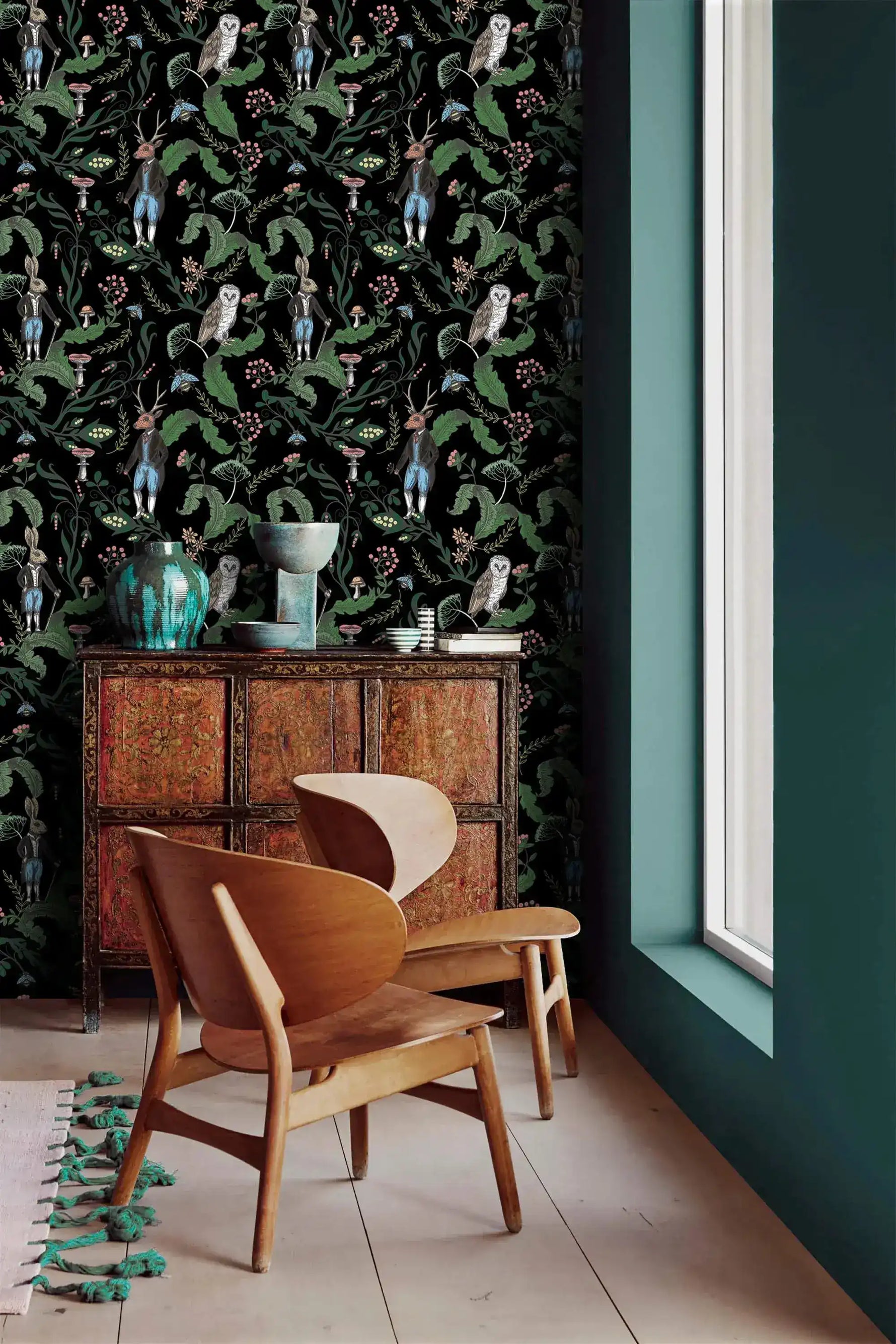 Dark woodland wallpaper with owls and hares on black beside a teal wall and carved wood cabinet