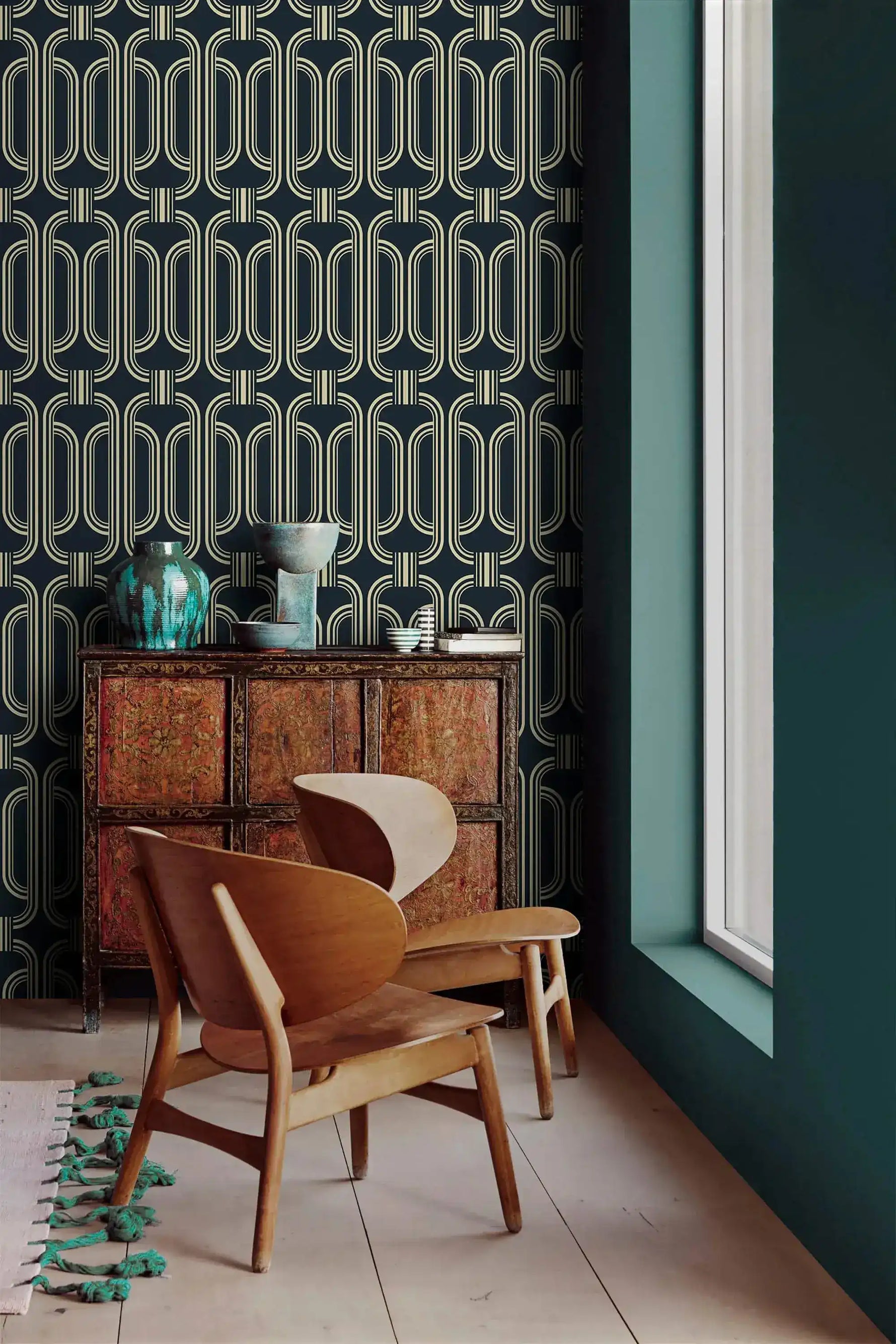 Deco geometric wallpaper with gold linked-oval lines on navy beside a teal wall and carved wood cabinet