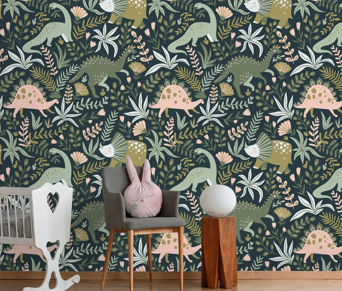 Dino Garden Oasis wallpaper with illustrated dinosaurs and tropical leaves on navy, shown in nursery with white crib.