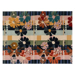 A vibrant, hand-tufted wool area rug featuring a colorful array of abstract flower designs in warm and cool tones. The Disco Daisies pattern showcases bold, graphic blooms set against a geometric backdrop, perfect for adding a playful touch to any room.