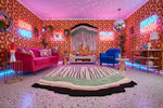 Colorful living room with an abstract wool rug, patterned walls, pink sofa, and neon signs.