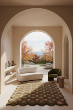 A modern interior scene framed by a large archway, showing a cream curved sofa, a dark green armchair, a patterned olive and pink rug, and an outdoor garden view beyond.