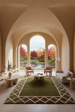 A large green area rug with a cream geometric border is styled in a modern, elegant living room with arched windows overlooking a garden pond and autumn trees.