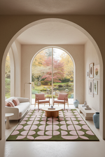 A modern living room with a large patterned area rug, two pink armchairs, and a white sofa, framed by a large arched doorway looking out to a garden scene.
