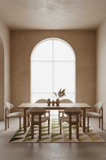 A minimalist dining room setup featuring a light wood rectangular table and four matching chairs with cream upholstery, arranged on a geometric patterned rug in front of a large arched window.