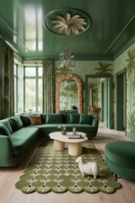A luxurious living room featuring a deep green sectional sofa, a matching green round ottoman, a patterned green and beige rug, and a white sheep figurine on the floor. The room has green walls with palm tree wallpaper, a large ornate gold-framed mirror, and a green ceiling with a decorative medallion.
