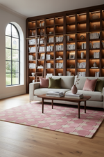 A styled living room featuring a large dark wood bookcase with built-in warm lighting, a light gray sofa with pink and olive pillows, a pink patterned rug, and a wooden coffee table on a light wood floor.