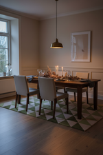 A dining room scene with a dark wood rectangular table set with white upholstered chairs, lit candles, and a green-and-white geometric patterned rug in a warm neutral interior.