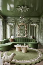 A luxurious green living room featuring a curved green sectional sofa, a matching round rug, a light wood coffee table, and a decorative sheep figurine in the foreground. The room has a glossy dark green ceiling with a palm tree motif, patterned wallpaper with palm trees, and arched windows.