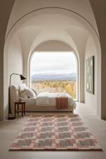 A modern bedroom with a large bed, pink and beige patterned rug, black floor lamp, and a massive arched window overlooking a forest and mountain landscape.