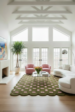 A modern living room with a large green and pink checkered rug, a white curved sofa, pink armchairs, a glass coffee table, and a tall potted plant in front of tall white-framed windows.