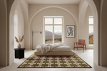 A styled bedroom interior with a platform bed, white bedding, a green and beige patterned area rug, a pink armchair, and arched walls framing a window view of mountains.