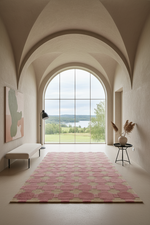 A pink and beige geometric patterned area rug displayed in a modern, arched entryway with a large window overlooking a green landscape.