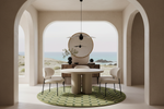 A modern dining room interior with a round white table, four cream chairs, a green patterned rug, and a large circular wall mirror, set within a beige arched structure overlooking a coastal landscape.