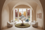 A modern interior scene with two curved cream sofas facing a round green rug and small central table, set in a large arched room with tall windows overlooking a garden pond and autumn trees.
