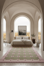 A large rectangular area rug with a green and pink plaid pattern and fringe, styled on a light floor in a modern, arched bedroom.
