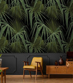 Green and black palm leaves wallpaper above dark wainscoting with retro mustard armchair and light wood sideboard