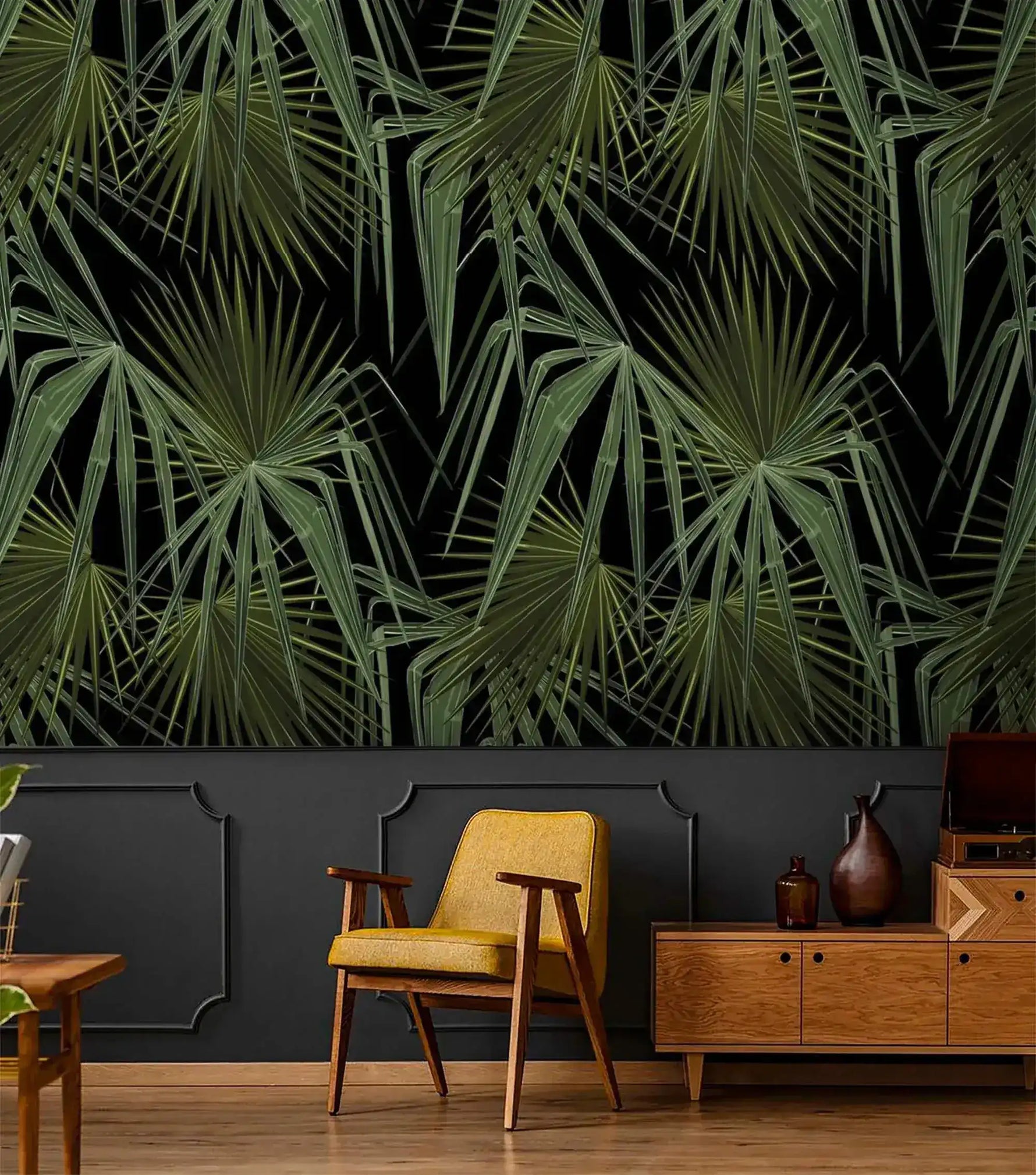 Green and black palm leaves wallpaper above dark wainscoting with retro mustard armchair and light wood sideboard