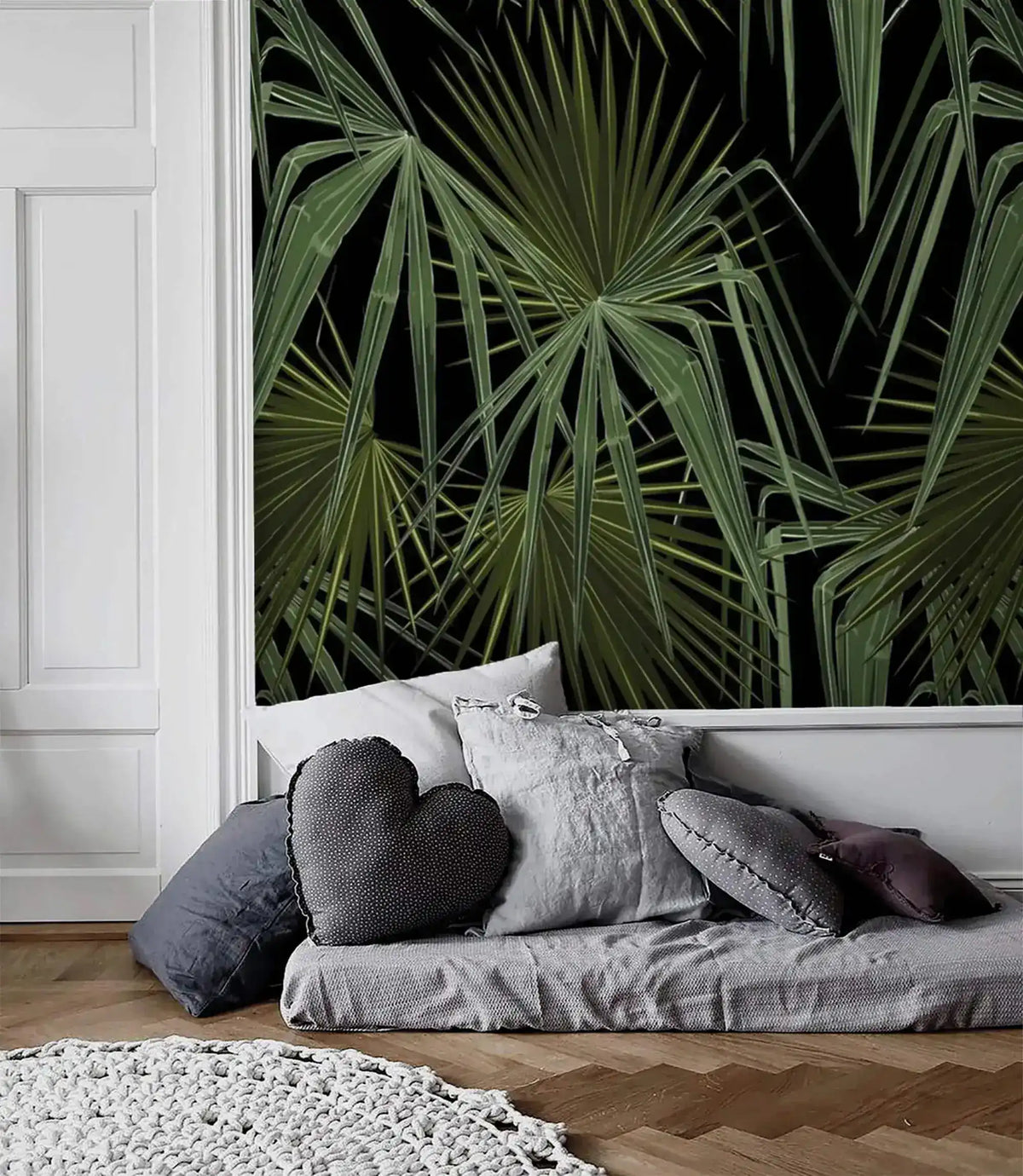Green and black palm leaves wallpaper panel in white-molded Scandi room with low grey daybed and heart-shaped cushion