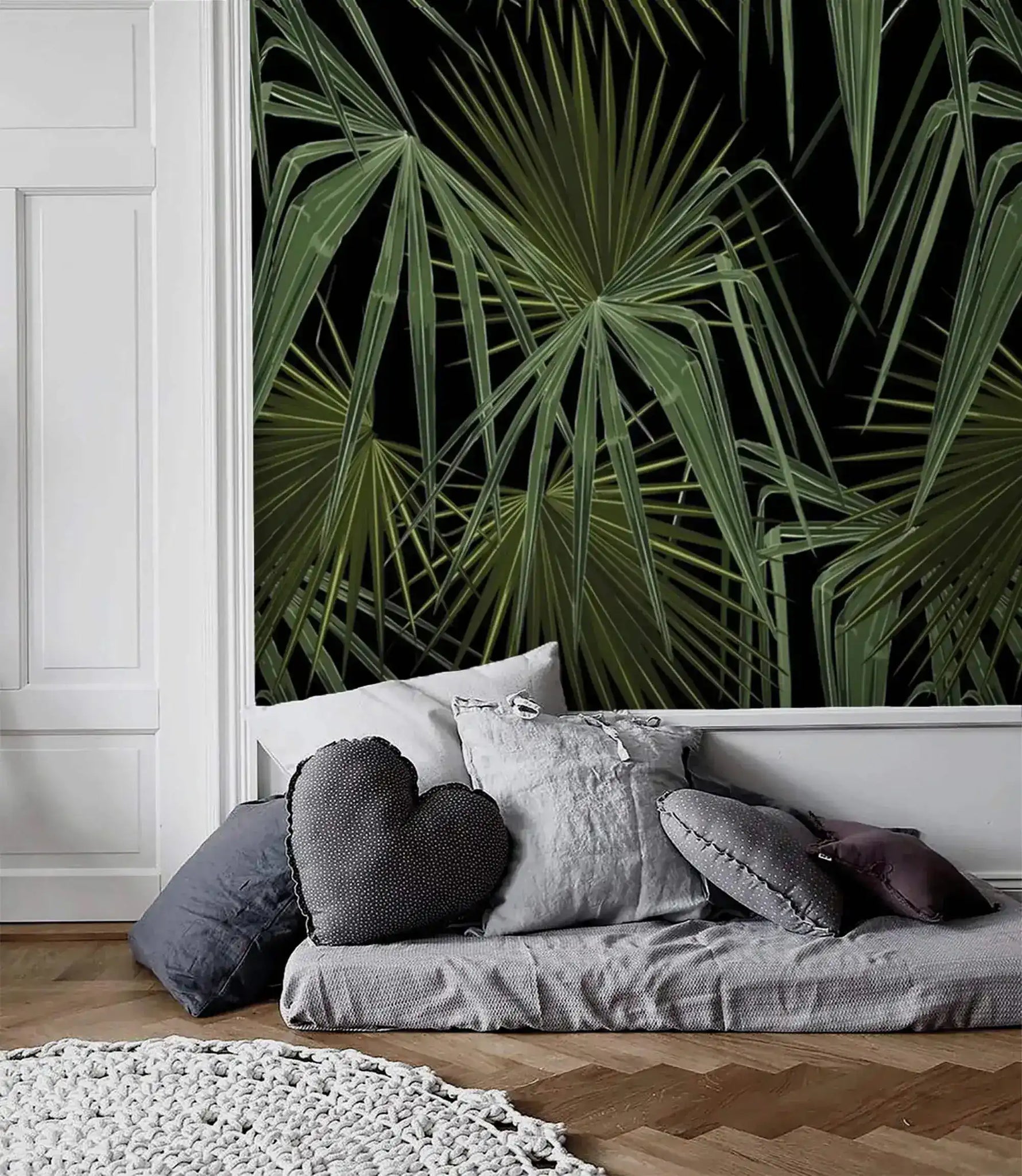 Green and black palm leaves wallpaper panel in white-molded Scandi room with low grey daybed and heart-shaped cushion