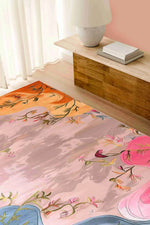 A vibrant Dreamscape Garden hand tufted area rug is beautifully displayed in a cozy bedroom setting. The wool rug features an abstract floral design with pink, orange, and blue hues, making it a perfect choice for adding artistic flair to an office or bedroom. This elegant piece is ideal for those seeking stylish and comfortable bedroom area rugs.