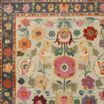 A vibrant, hand-knotted area rug featuring an intricate floral pattern in various colors. The design is framed by a decorative border with a rich blue background, enhancing the lively and detailed floral motifs.