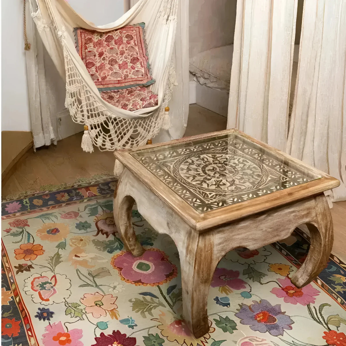 A cozy living space featuring a Dreamy Floral Hand Knotted Area Rug with vibrant floral patterns, complemented by a rustic wooden coffee table with intricate carvings. A hammock with a decorative pillow is suspended nearby, creating a warm and inviting atmosphere.