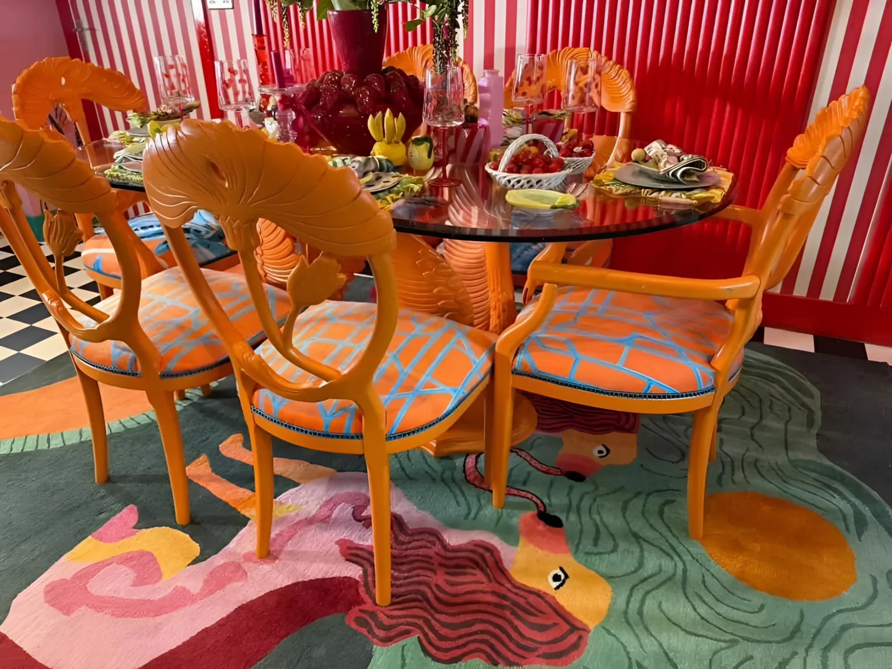 A vibrant Duo Tails Hand Tufted Area Rug adding a contemporary flair to a dining room with bold orange chairs and a glass table. The wool rug features an abstract design, perfect for modern bedrooms or offices, making it an ideal choice for office rugs.