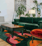 A stylish living room featuring a Duo Tails Hand Tufted Area Rug with a vibrant abstract design. The contemporary wool rug adds a pop of color under the wooden coffee table and velvet green sofa, perfect for a modern bedroom or office setting.