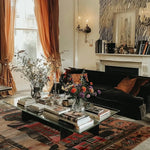 A cozy living room featuring the Egyptian Enigma Wool Hand Knotted Area Rug. This vintage rug showcases intricate patterns and rich colors, adding warmth and character to the space. Perfect for those seeking elegant rugs for living room decor, this area rug complements a stylish black sofa and a glass coffee table adorned with books and flowers.