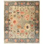 The Elysian Bloom Knotted Wool Area Rug features an intricate floral design with vibrant pink and orange flowers set against a muted beige background. The outer border showcases a contrasting deep blue tone with additional floral accents, adding a touch of elegance to any living space.
