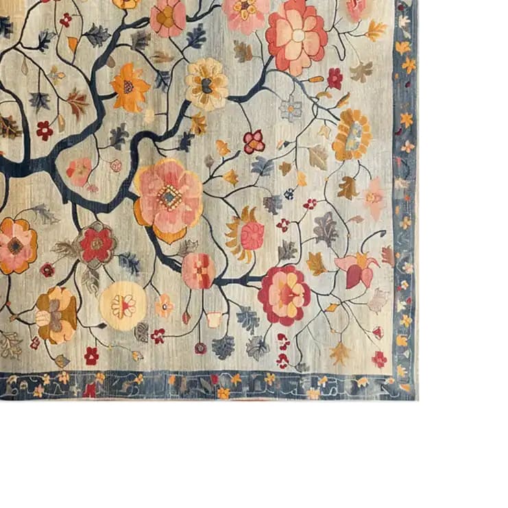 A vibrant area rug featuring a detailed floral pattern with colorful blooms and leaves on a light background. The intricate design showcases a rich tapestry of pink, orange, and yellow flowers intertwined with dark, flowing branches. A decorative border with floral motifs frames the rug, adding an elegant touch.