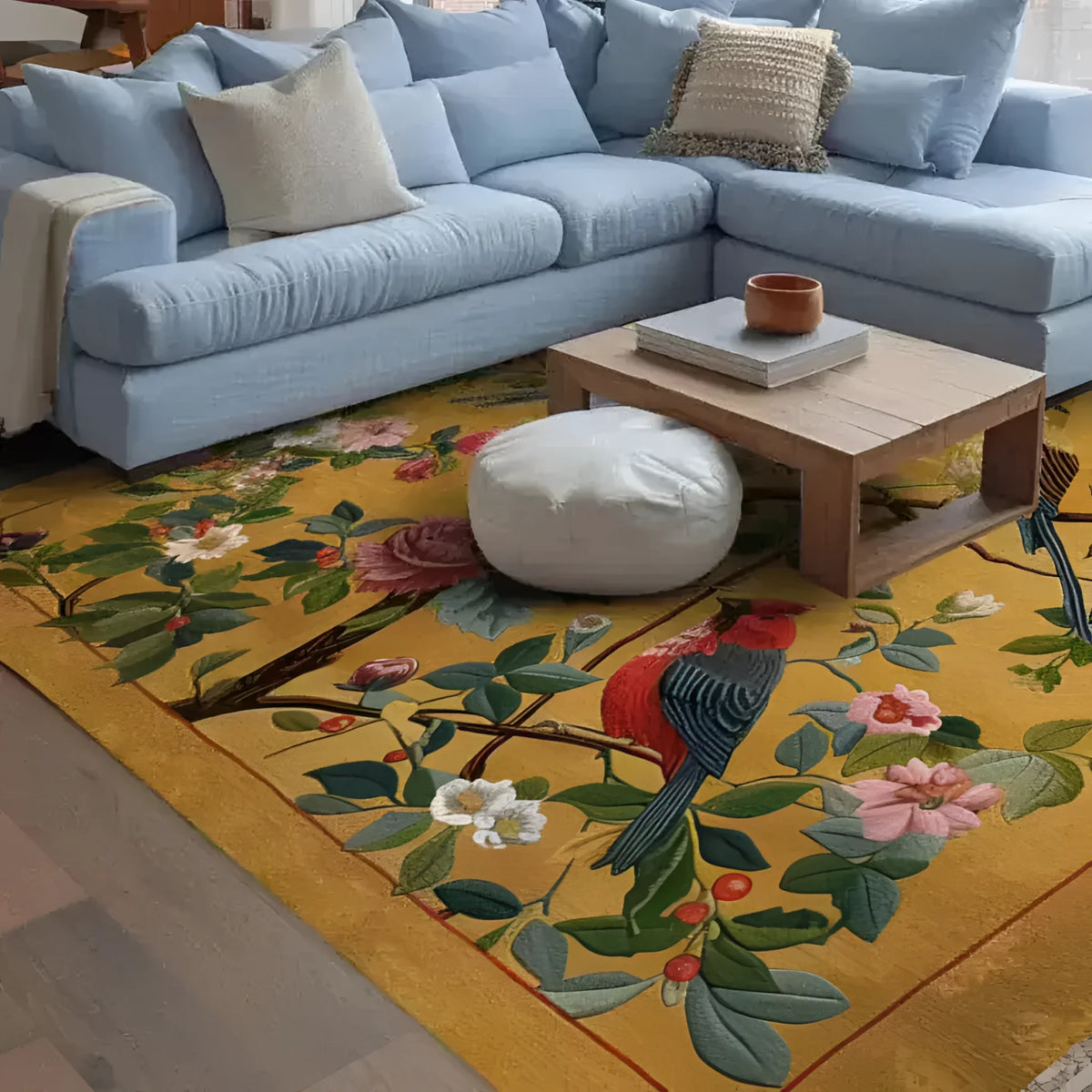 A vibrant Emperor's Loom Hand Tufted Area Rug adorns a cozy living room, featuring a detailed floral and bird design on a warm yellow background. This wool rug complements a light blue sectional sofa and wooden coffee table, creating an inviting and stylish space for large living room settings.